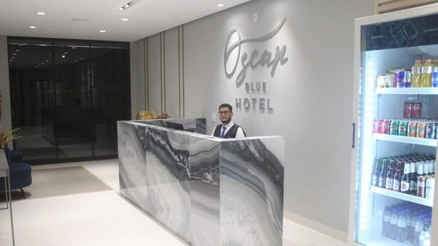 En receptionsdisk med marmorimitation, ett kylskåp fyllt med drycker och en vägg med hotellets namn.