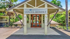 Entrada de un resort rodeada de palmeras, con un letrero que dice 'Port Douglas Sands Resort' y un cielo despejado.