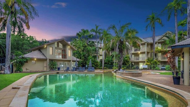 Una piscina rodeada de palmeras y un edificio con varios balcones.