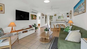 Una sala moderna con un televisor de pantalla plana, un sofá verde, una mesa de comedor y una cocina al fondo.
