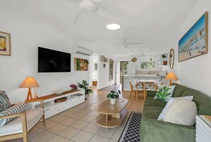 Ein modernes Wohnzimmer mit Flachbildfernseher, einem grünen Sofa, einem Esstisch und einer Küchenzeile im Hintergrund.
