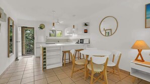 Una cocina moderna con armarios blancos, un comedor con sillas blancas, un espejo redondo y un ventilador de techo.