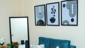 Un canapé de couleur turquoise orné de coussins à motifs, un grand miroir et une œuvre d’art abstraite accrochée au mur.