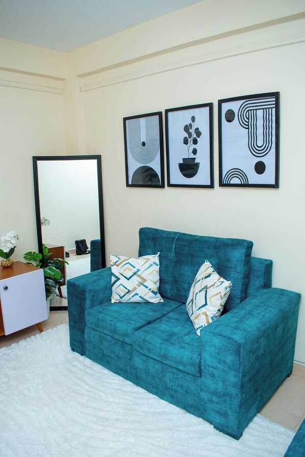 A teal sofa with patterned cushions, a large mirror, and abstract artwork on the wall.