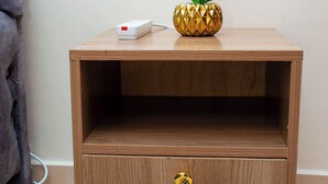 Une table de chevet en bois, dotée d’un tiroir, d’une multiprise et d’un ananas décoratif.
