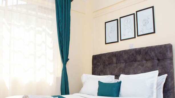 Un lit avec une tête de lit capitonnée, un couvre-lit blanc et des coussins turquoise.