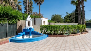 Un patio con una fuente, palmeras y un pequeño edificio blanco con una estatua.