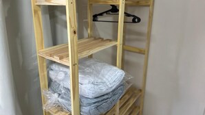 Une étagère en bois, composée de plusieurs étagères, dont certaines supportent des objets, et un cintre noir est accroché à l’une d’elles.