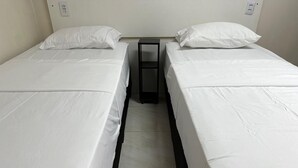 Une chambre double avec deux lits simples, une petite table et une prise de courant au mur.
