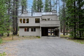 A two-story house with a garage, surrounded by tall pine trees.