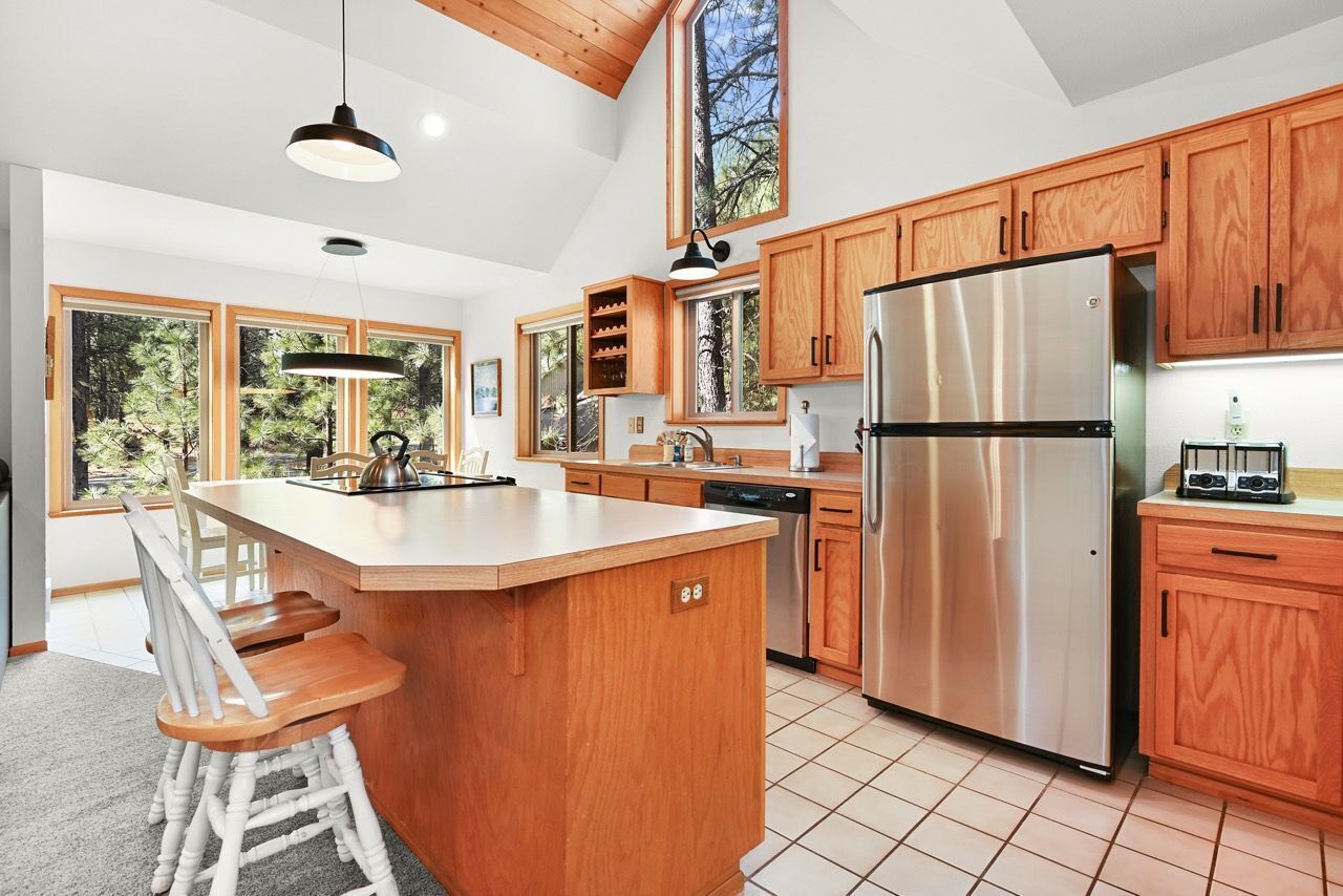 A modern kitchen with wooden cabinets, a stainless steel refrigerator, and a large island with bar stools.