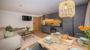 A modern living room with a sofa, a coffee table, and a dining area with a table set for two. - Lennis Apartments - Top 2, Terrace, Mountain View (Bruck an der Großglocknerstraße)