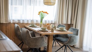 A dining area with a wooden table, four grey chairs, a vase with flowers, and a woven basket. - Lennis Apartments - Top 2, Terrace, Mountain View (Bruck an der Großglocknerstraße)