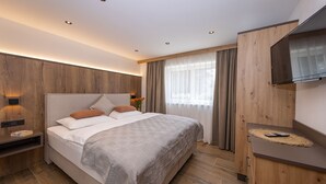 A modern bedroom with a large bed, wooden panel walls, a bedside table, a TV, and a window with curtains. - Lennis Apartments - Top 2, Terrace, Mountain View (Bruck an der Großglocknerstraße)