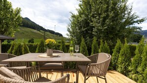 An outdoor deck with a table and chairs, surrounded by greenery and a mountainous backdrop. - Lennis Apartments - Top 2, Terrace, Mountain View (Bruck an der Großglocknerstraße)