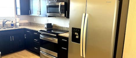 A kitchen with dark cabinets, stainless steel appliances, a microwave, oven, and a refrigerator.