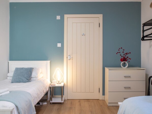A bedroom with two beds, a bedside table with a lamp, a dresser, and a door.