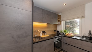 Una cocina moderna con armarios grises, un lavamanos de acero inoxidable y una ventana con vistas a árboles.