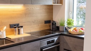 Una cocina moderna con protector de pared de madera, estufa empotrada, horno y ventana con vista a árboles.