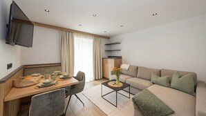 Una sala de estar moderna con un sofá, una mesa de comedor con sillas, un televisor montado en la pared y una zona de cocina con armarios.