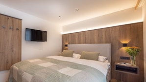 Un dormitorio moderno con una cama grande, paneles de madera, una televisión montada y una mesita de noche con un florero.