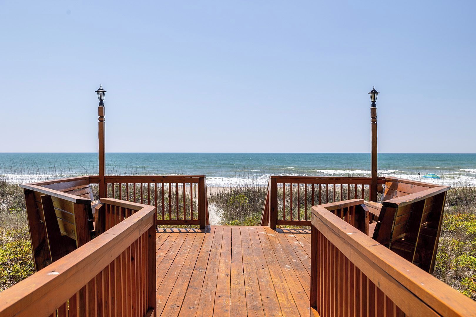 Eine Holzterrasse mit Geländern, die auf einen Strand blickt.