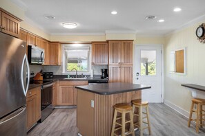 Una cocina moderna con armarios de madera, un refrigerador de acero inoxidable, horno empotrado, un lavaplatos y un ventanal.