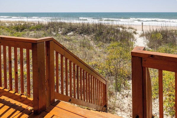 A wooden deck leading to a beach with a sandy path and vegetation. - Lou Sea Ann West, Oceanfront Duplex - 4BR 2BA (Emerald Isle)
