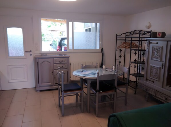 A compact room with a dining table, chairs, a radiator, a window with a view, and a metal shelf unit.