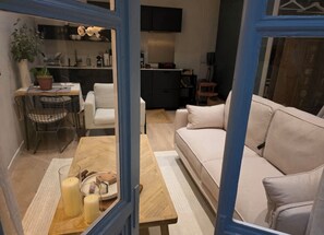 Een moderne woonkamer met een bank, een eettafel met stoelen, een keukenhoek en een aan de muur bevestigde televisie.