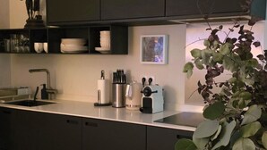 Una cocina moderna con armarios oscuros, una encimera blanca, un fregadero, una cafetera y una planta en maceta.