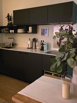 Una cocina moderna con armarios oscuros, una encimera blanca, un fregadero, una cafetera y una planta en maceta.
