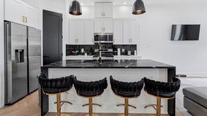 Une cuisine moderne dotée d’appareils électroménagers en acier inoxydable, d’un îlot central et de tabourets de bar noirs.