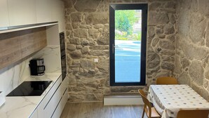 A compact kitchen with a stone wall, a dining table with chairs, and a window with a view of greenery.