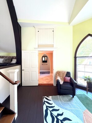 A room with a staircase, a black armchair, a patterned rug, and a window with a view. - Unique loft space 500 ft from Salmon River! (Altmar)