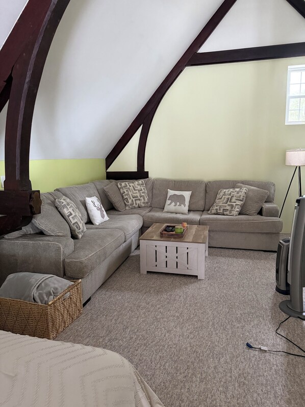 A cozy loft-style room with a sectional sofa, a small wooden coffee table, and a television.