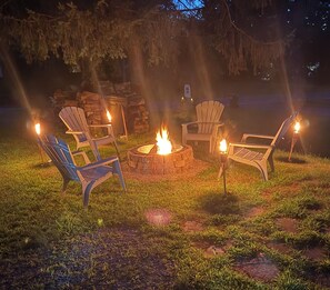 A fire pit with chairs around it, set in a grassy outdoor area at night.