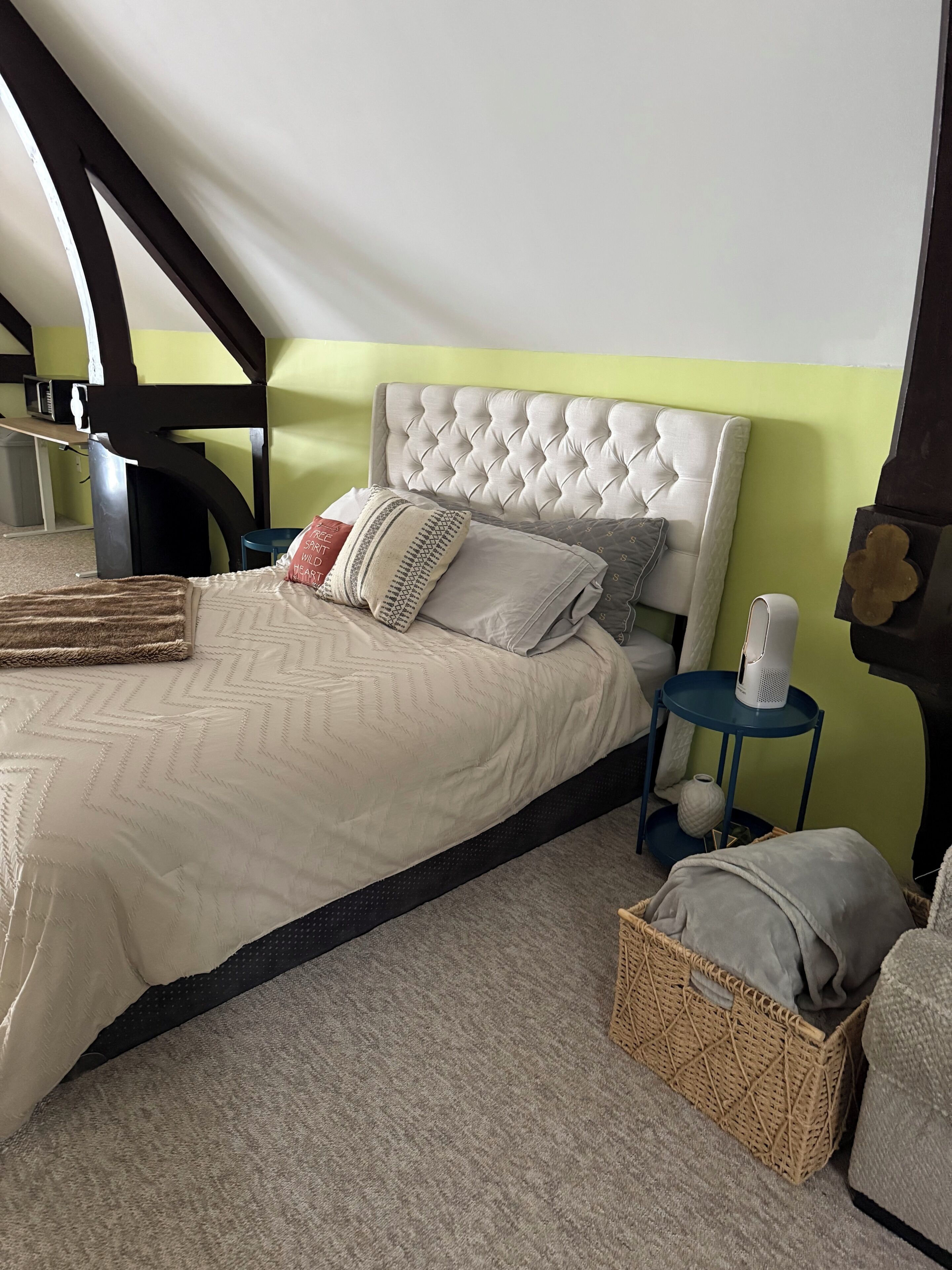 A neatly made bed with a tufted headboard, a bedside table with a lamp, and a wicker basket on the floor.