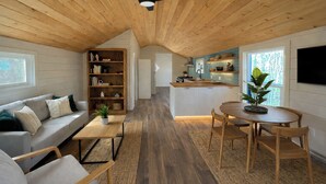 Un intérieur chaleureux avec un plafond en bois, un espace de vie comprenant un canapé et une table basse, une cuisine avec un bar et un coin repas avec des chaises.