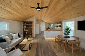Ein gemütliches Interieur mit Holzbalkendecke, einem Wohnbereich mit Sofa und Couchtisch, einer Küche mit Bar und einem Essbereich mit Stühlen.