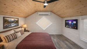 Une chambre à coucher avec un lit, un ventilateur de plafond, un téléviseur fixé au mur et un tableau accroché au mur.