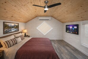 Ein Schlafzimmer mit einem Bett, einem Deckenventilator, einem an der Wand befestigten Fernseher und einem Bild.
