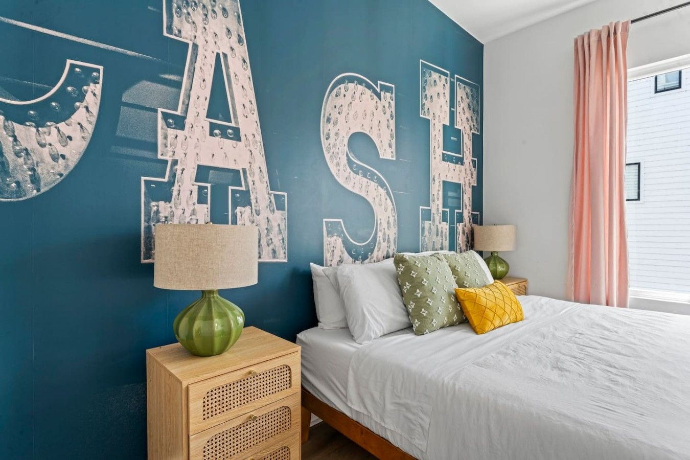 Une chambre à coucher avec un lit, une table de chevet, une lampe et un mur orné de grandes lettres.