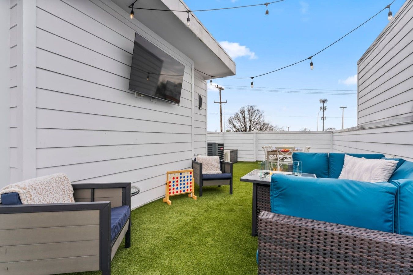 A backyard with a white house, outdoor furniture, a fire pit, and a children's game set.