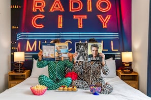 A room with a bed, two bedside tables, a neon sign, and magazines. - Rhythm & Roots Retreat (Nashville)