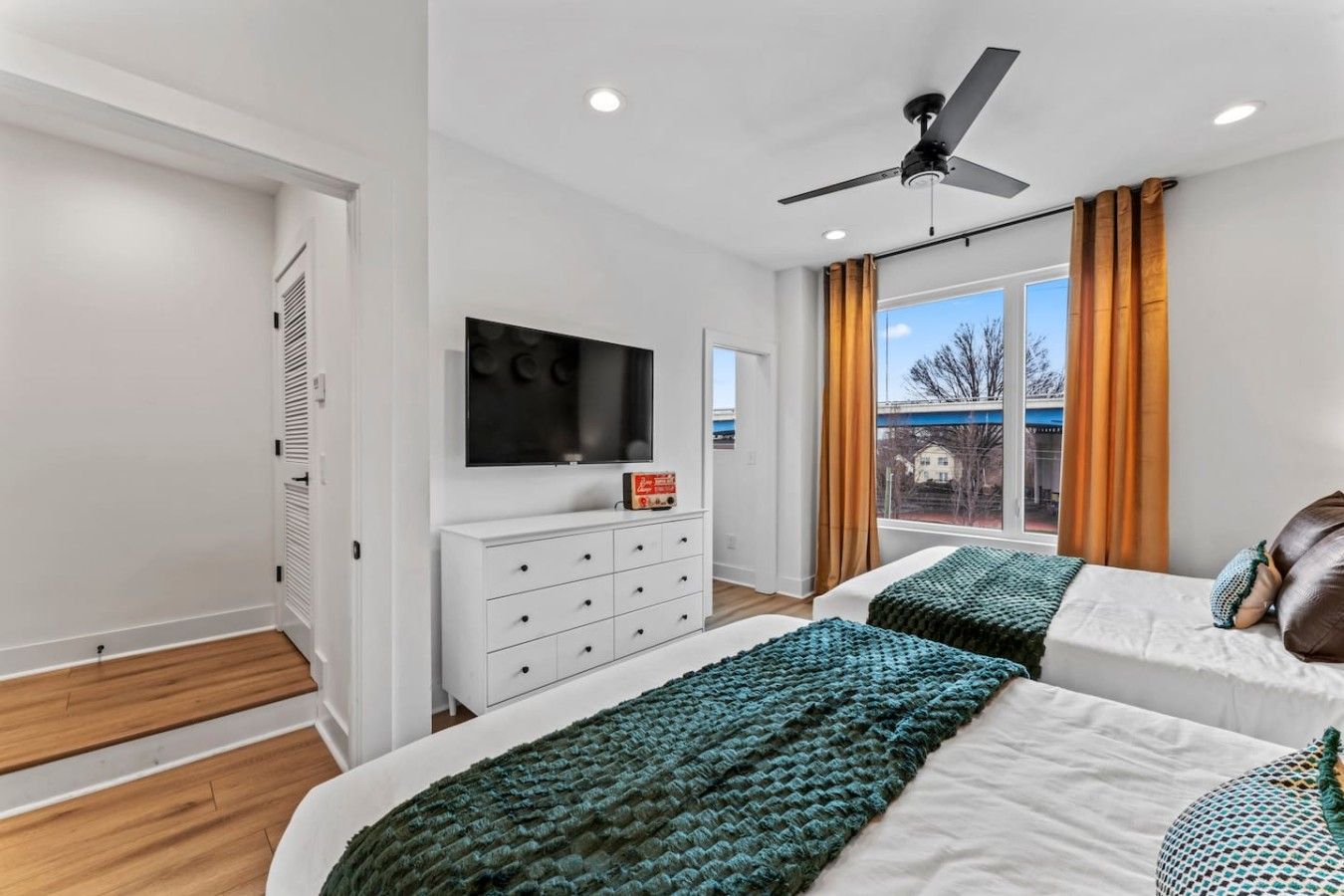 A modern bedroom with two beds, a TV, a white dresser, and a ceiling fan.