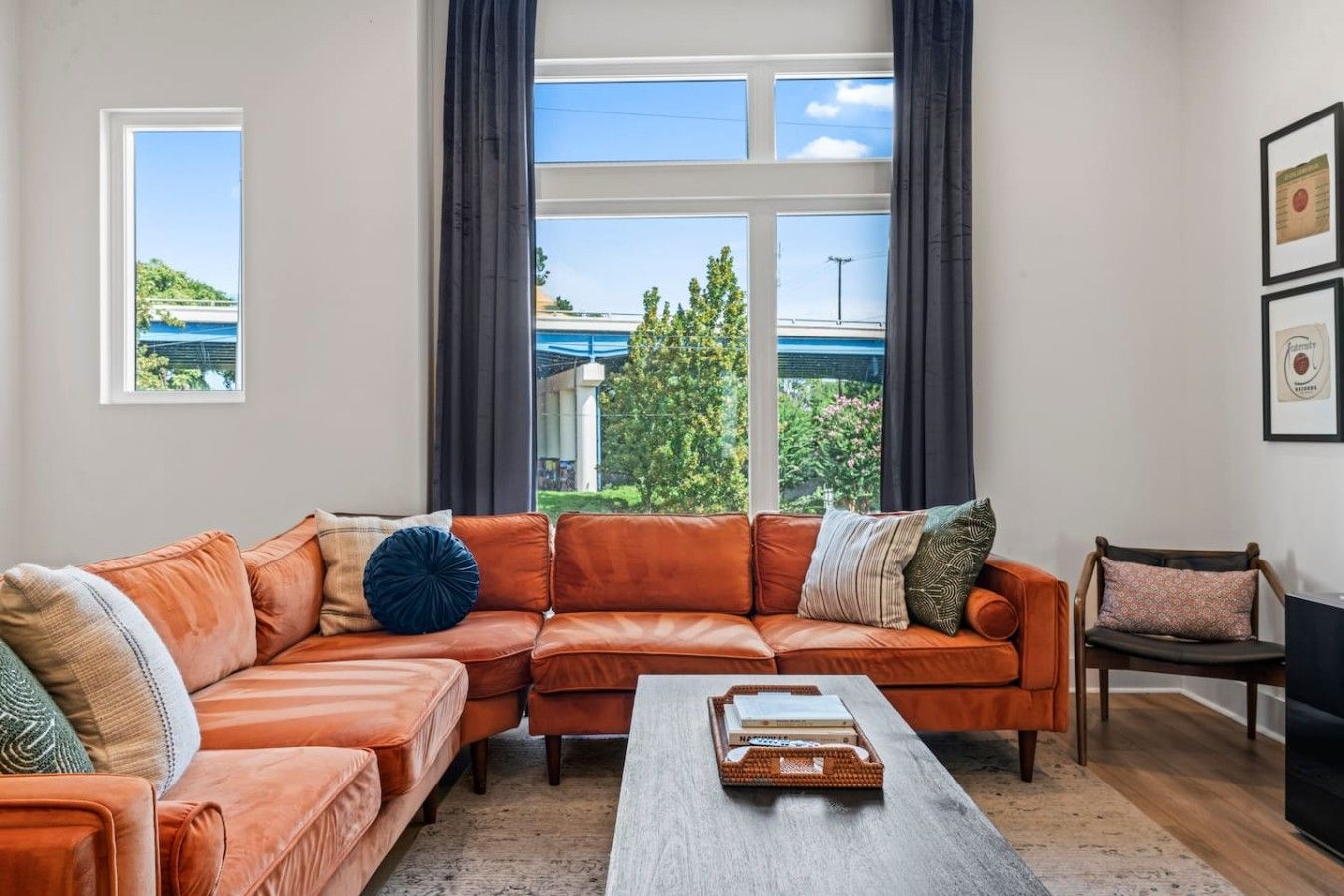 A living room with a sectional sofa, a coffee table, and a view of a bridge and greenery outside.