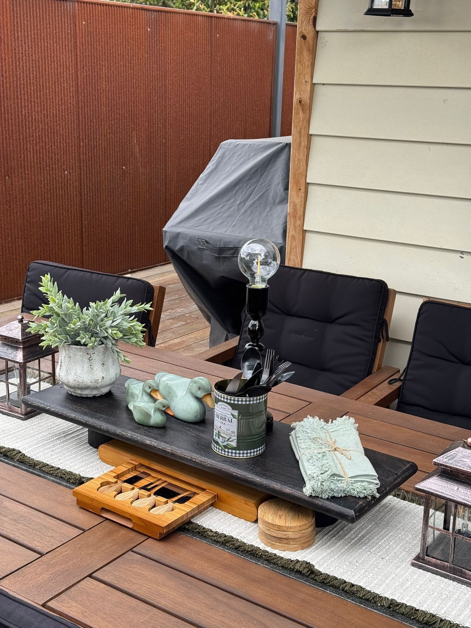 An outdoor dining area with a table set for two, featuring a potted plant, a tea pot, and a lantern.