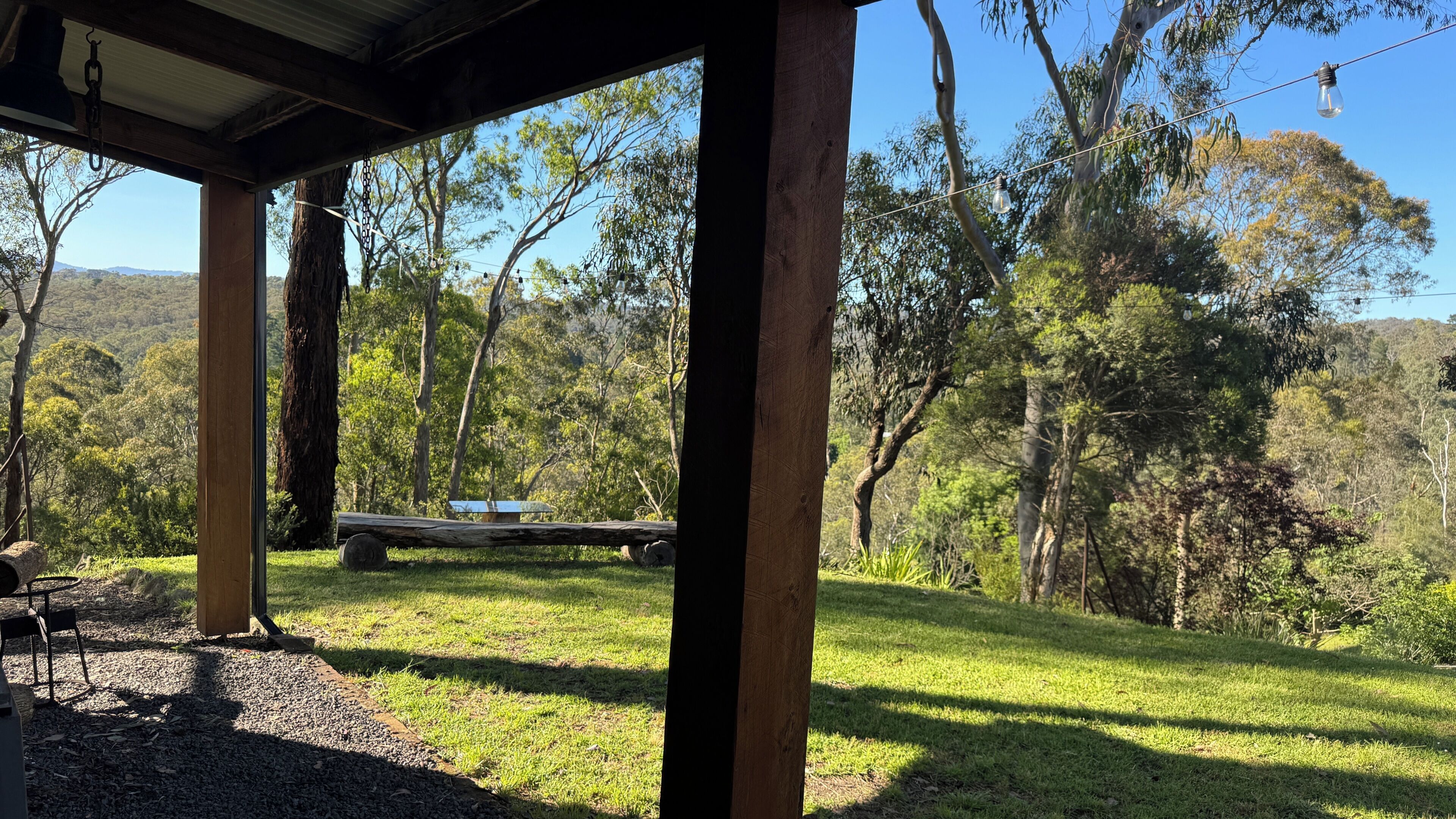 Un espacio al aire libre cubierto, con una mesa y sillas, rodeado de árboles y un paisaje cubierto de césped.