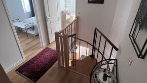 A staircase with a wooden handrail and a metal banister, leading to a room with a bed and a window. - House two minutes from the beach (barfleur)